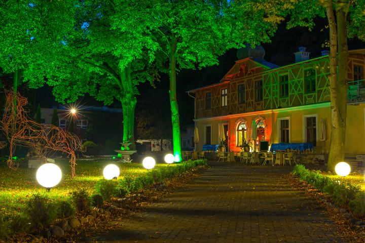 A pathway illuminated by glowing orbs and vibrant green trees near a building.