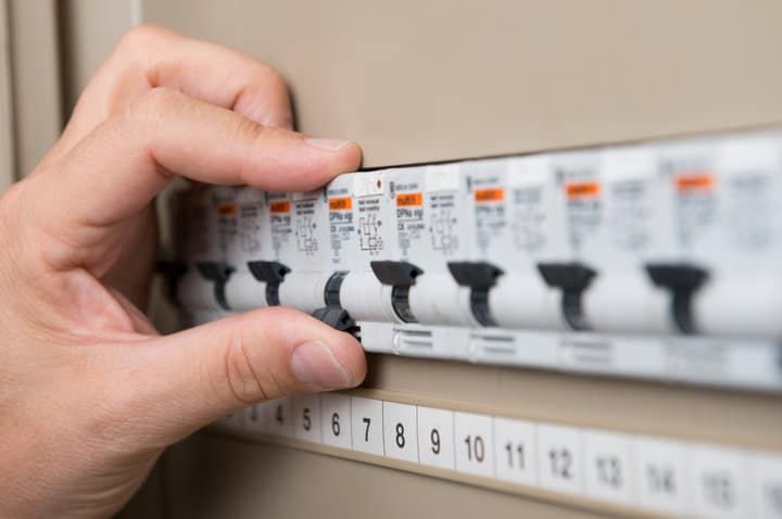 A hand adjusting circuit breakers on a home electrical panel.