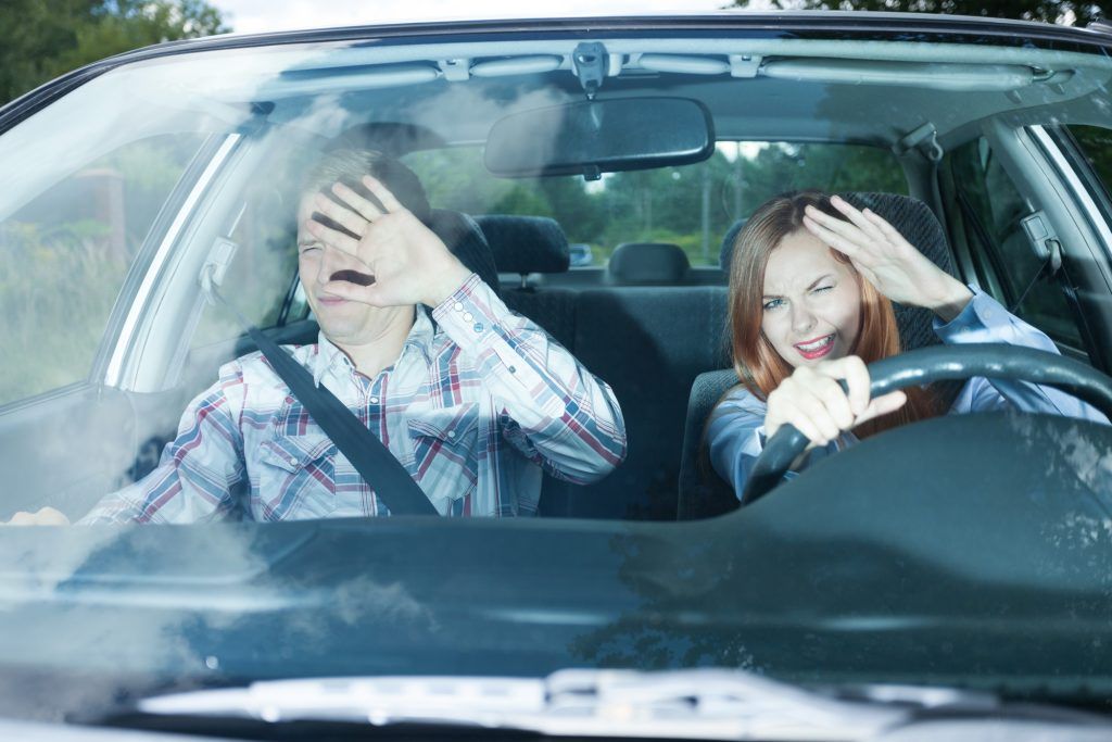 Frustrated driver and passenger shielding their eyes from bright sunlight.