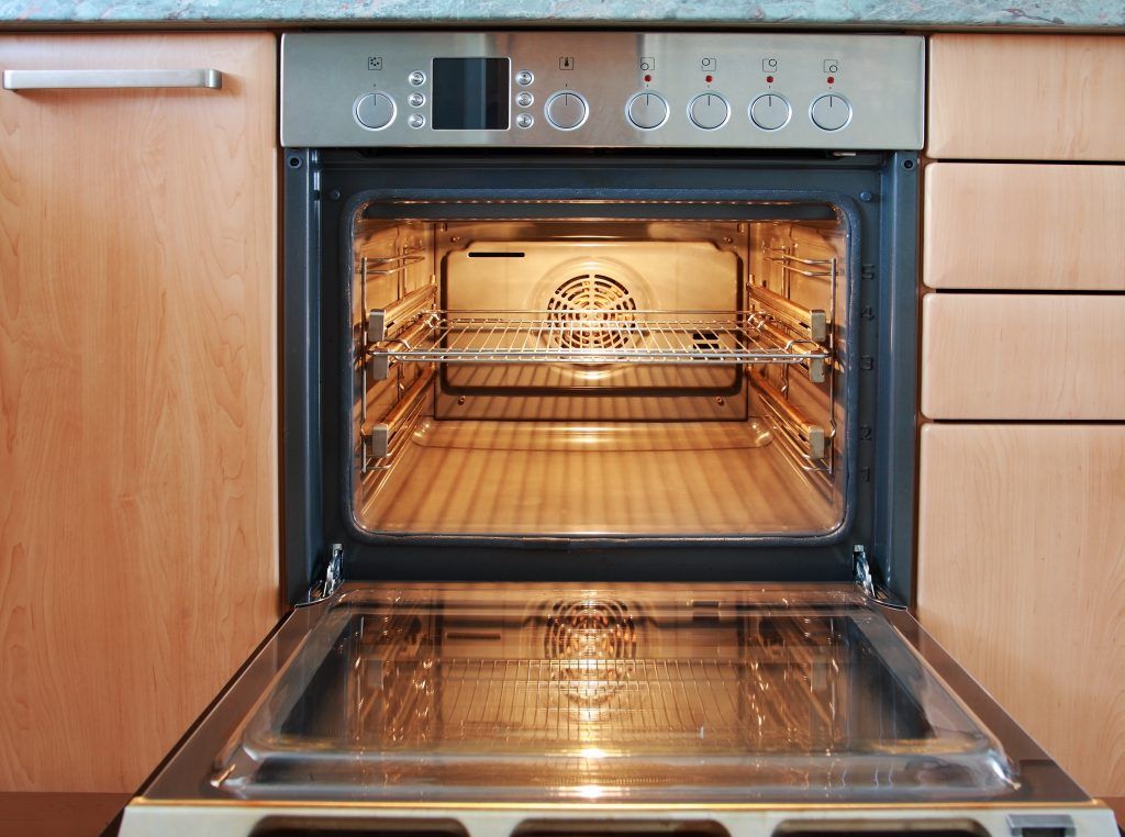A modern kitchen oven with open door displaying empty racks inside.