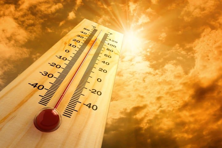 A close-up of a thermometer against a bright, cloudy sky.