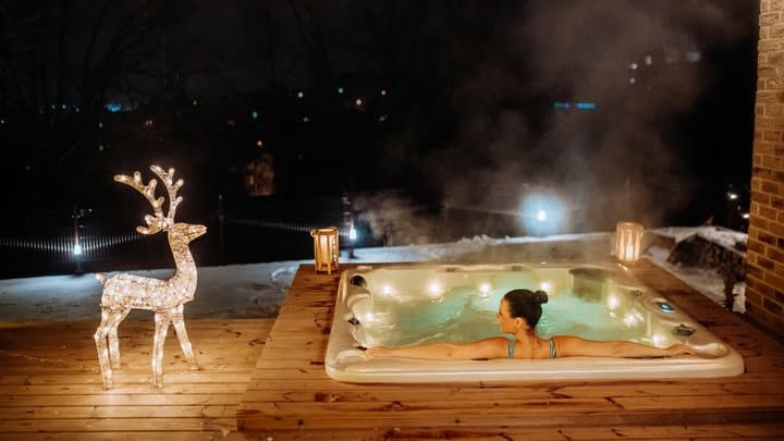 A woman relaxes in a hot tub surrounded by winter decor and glowing lights.