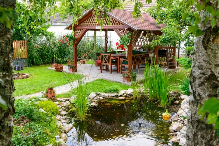 Cozy garden with a wooden gazebo and pond surrounded by lush greenery.