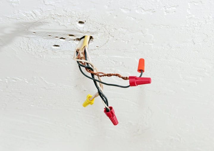 Exposed electrical wires with colored wire connectors against a ceiling.