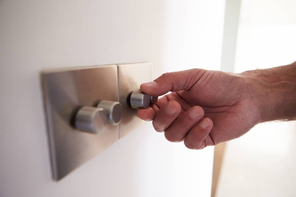 A hand adjusting a dimmer switch on a wall for LED lighting.