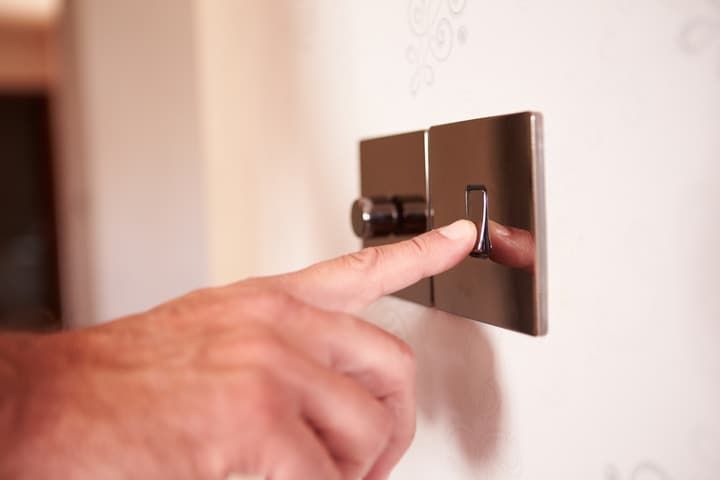 A hand pressing a modern light switch on a wall.