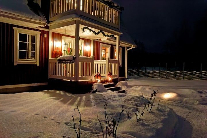 Cozy house exterior adorned with string lights and snow at night.