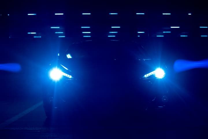 A car illuminated by bright blue LED headlights in a dark environment.
