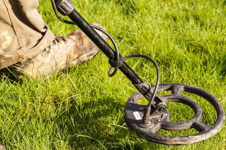 A metal detector resting on grass with a person in boots nearby.