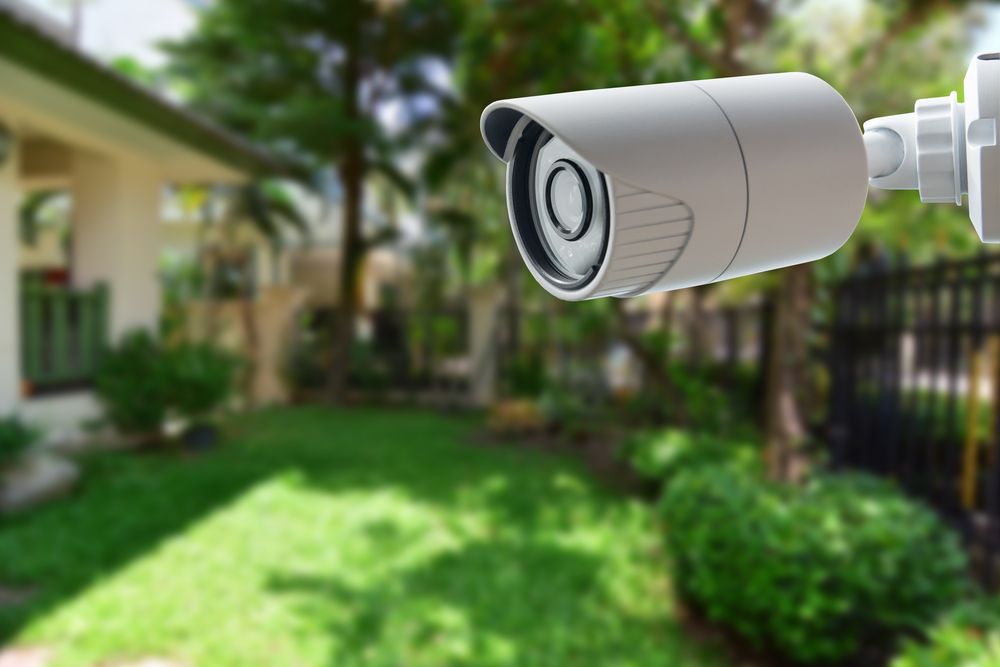 A security camera mounted near a green lawn and landscaped area.