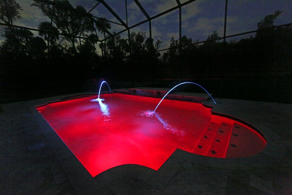 A brightly illuminated pool at night with red and blue lighting effects.
