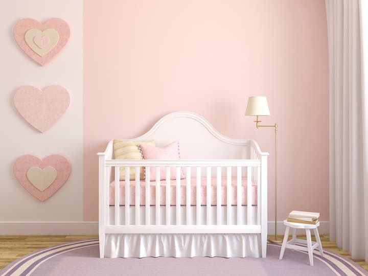 A cozy nursery with a white crib, soft pink walls, and heart decor.