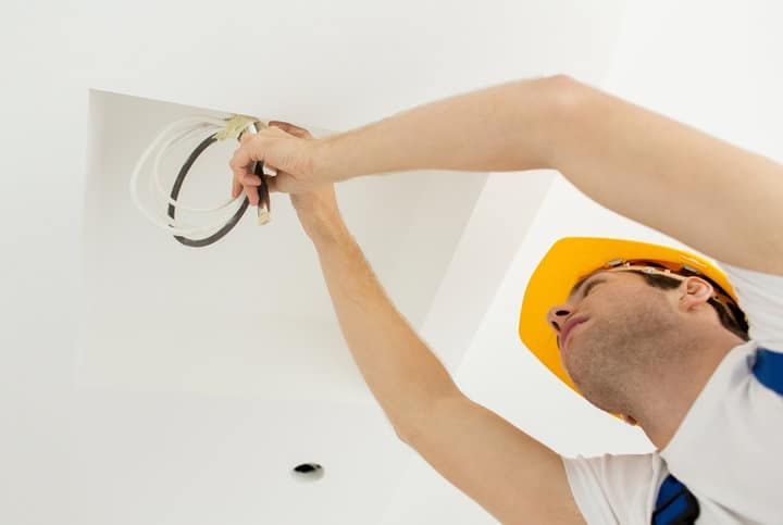 A worker installs wiring in a ceiling for LED lighting.