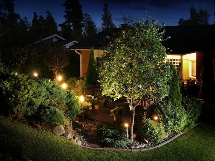 Well-lit garden with a cozy deck, surrounding trees, and glowing lights.
