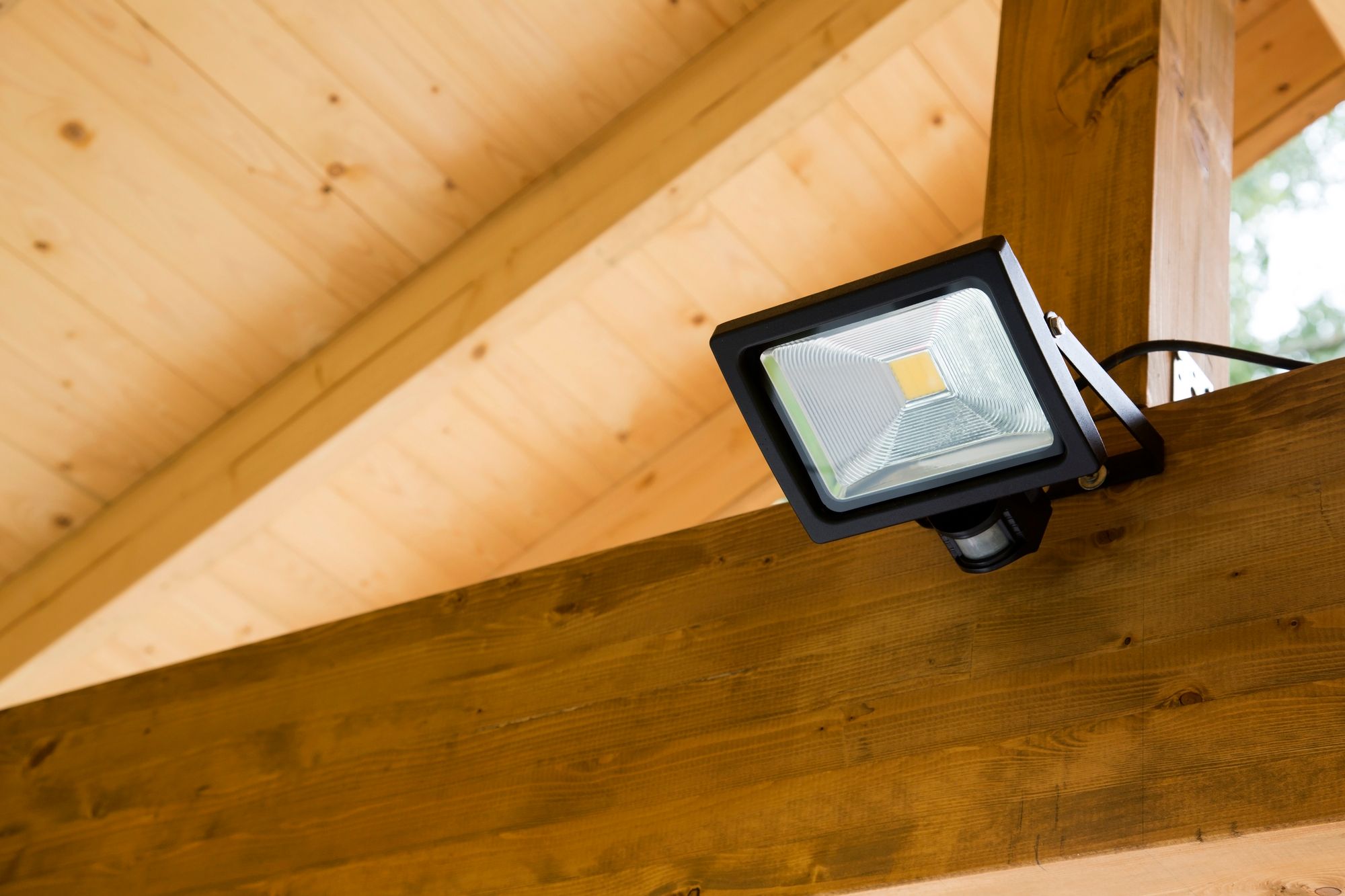 A black LED floodlight mounted on a wooden beam indoors.