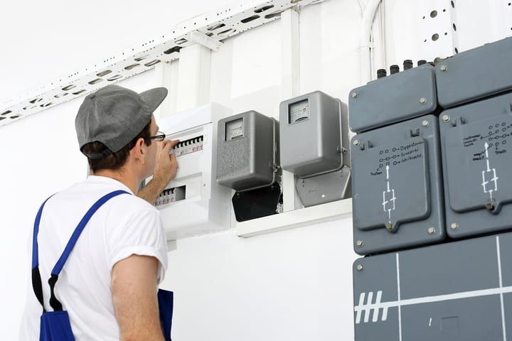 Technician checking electrical meters and circuit breakers on a wall.