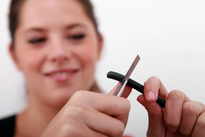 A woman uses scissors to trim a black cable or wire.