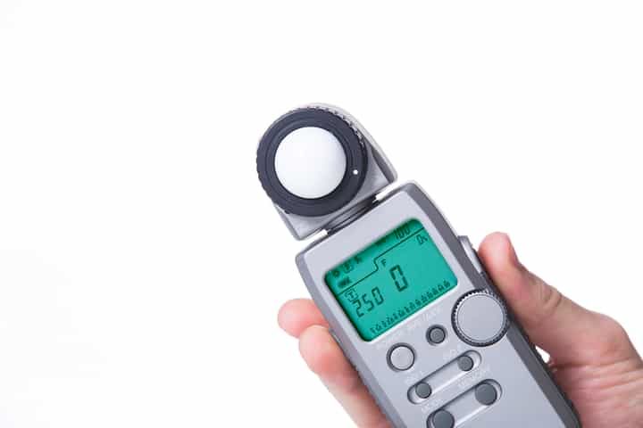 Hand holding a light meter with digital display and measurement sphere.