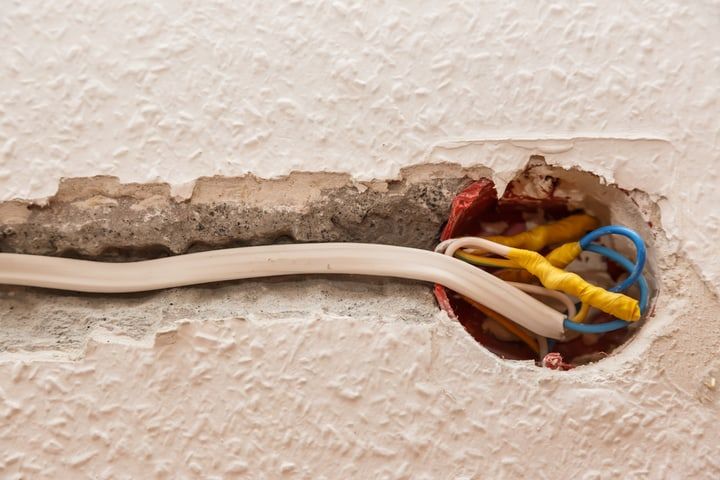Exposed electrical wires in a wall opening with a crack.