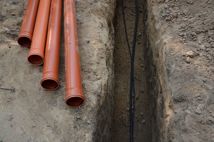 A trench filled with electrical cables and orange pipes on the side.