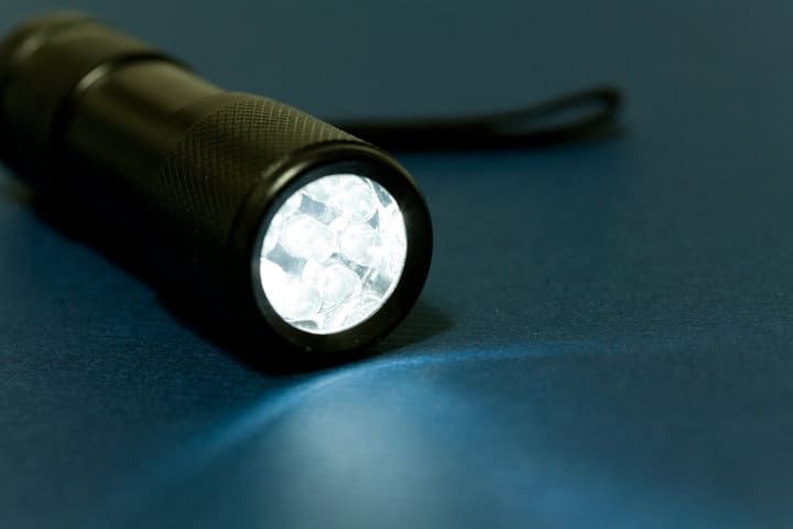 A black flashlight with bright LED bulbs illuminating a blue surface.