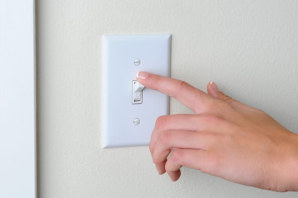A hand pressing a light switch on a wall to turn on the light.