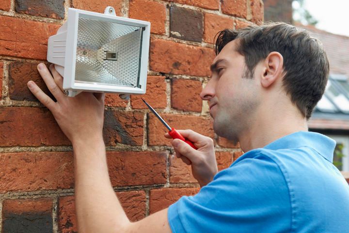 A man installs an LED light fixture on a brick wall.