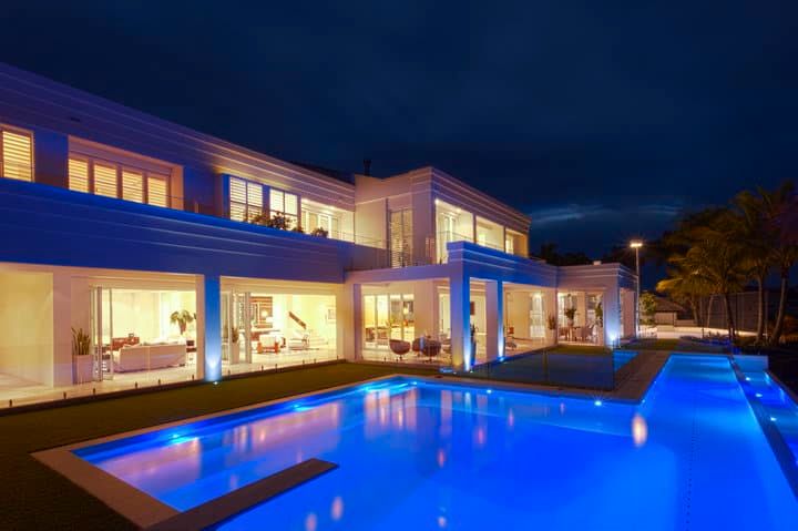 Modern villa illuminated with blue LED lights beside a swimming pool at night.