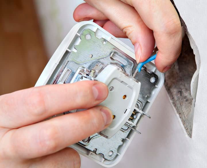 Hands installing a white electrical outlet into a wall socket.
