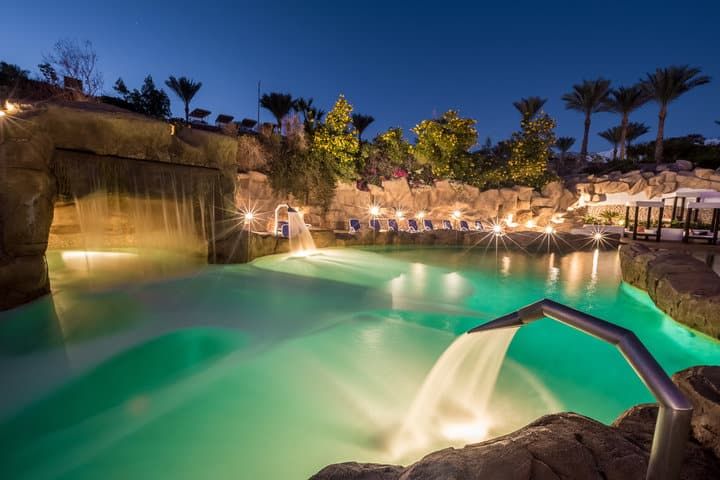 A tranquil pool scene with cascading waterfalls and glowing lights at dusk.