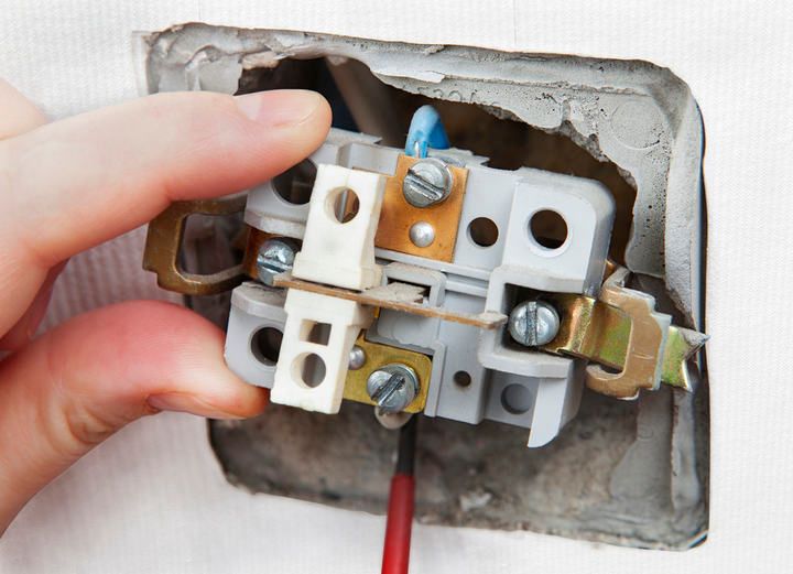 A hand adjusting the wiring of an electrical connector in a wall.