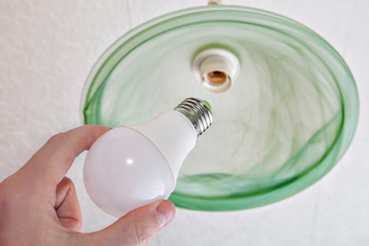 A person holding a white LED light bulb beneath a green lampshade.