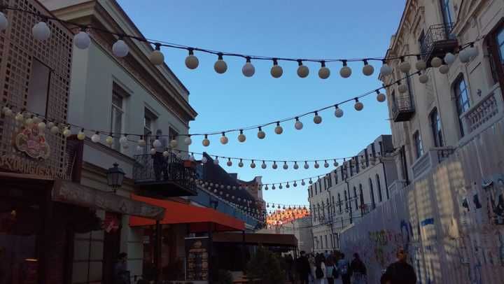 A street lined with buildings and decorative LED string lights overhead.