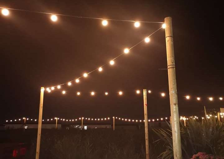 String lights illuminate a dark outdoor space with wooden posts.