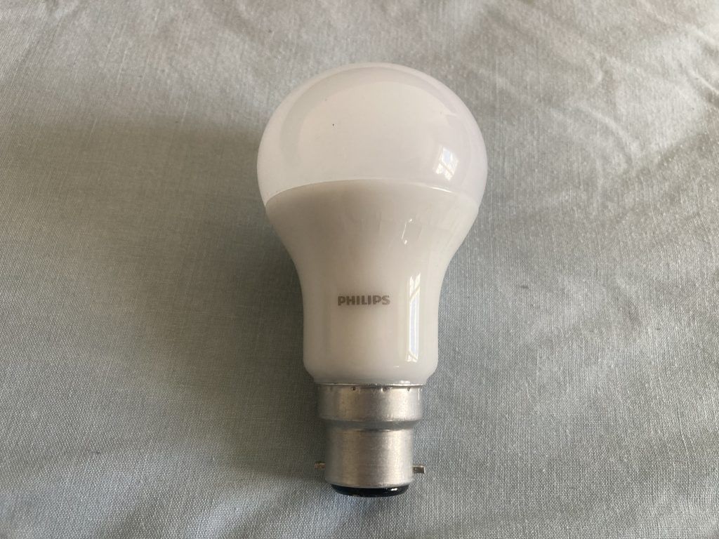 A Philips LED light bulb with a rounded top on a soft fabric background.