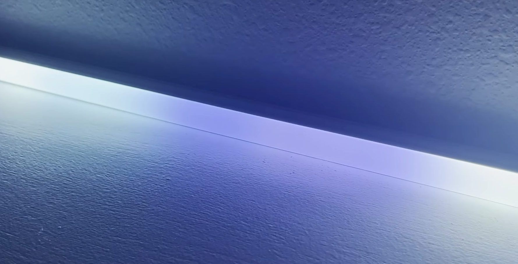 LED strip light emitting a soft blue glow along a textured wall.