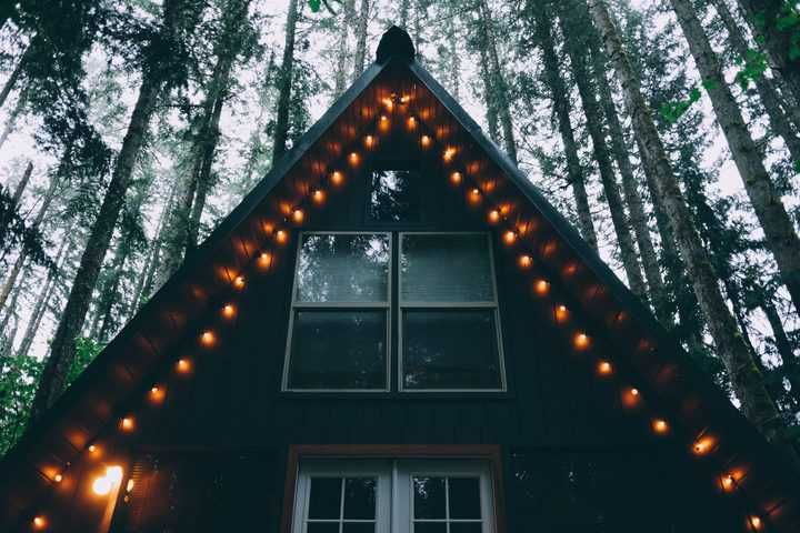 Cozy cabin exterior illuminated with warm LED lights among tall trees.