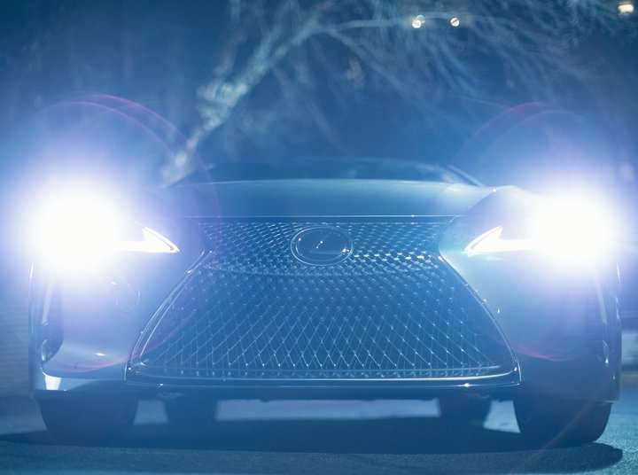 A luxury car with bright LED headlights illuminating a dark area at night.