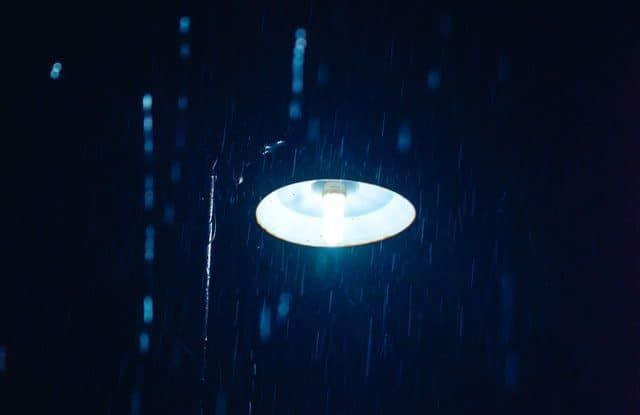 A glowing LED light illuminates rain falling in a dark environment.