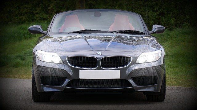 A sleek gray convertible car with bright headlights, parked on a street.