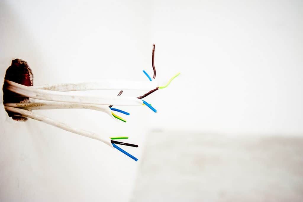 Colorful electrical wires emerging from a hole in a white wall.