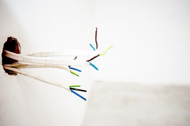 Electrical wires with various colors protruding from a wall opening.