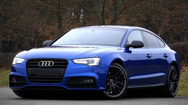 A sleek blue Audi car parked on a road with trees in the background.