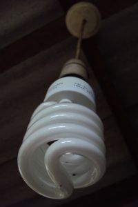 A compact spiral LED light bulb hanging from a ceiling fixture.