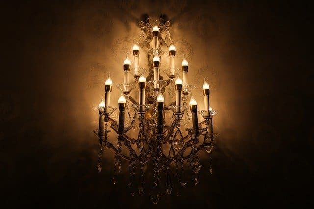 A lavish chandelier with multiple bright bulbs illuminating a dark background.