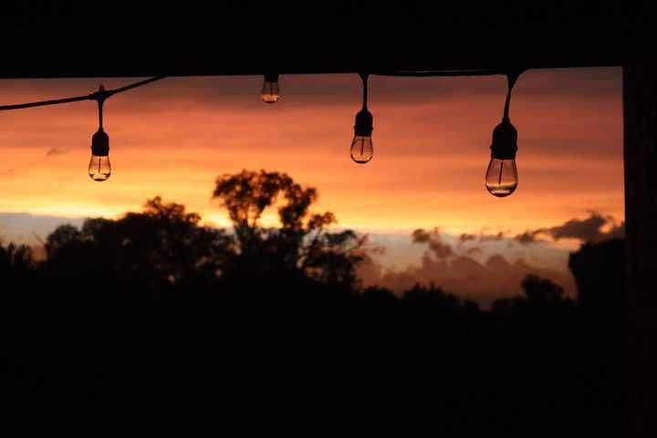 String lights hanging against a colorful sunset with silhouettes of trees.