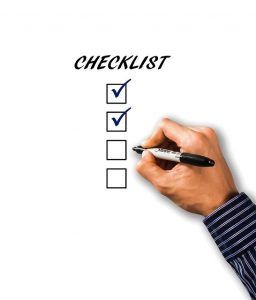 A hand writing on a checklist with three checked boxes.