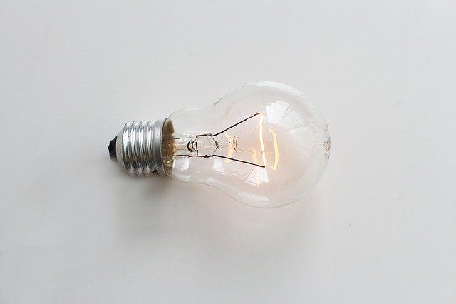 A glowing incandescent light bulb laying on a white surface.