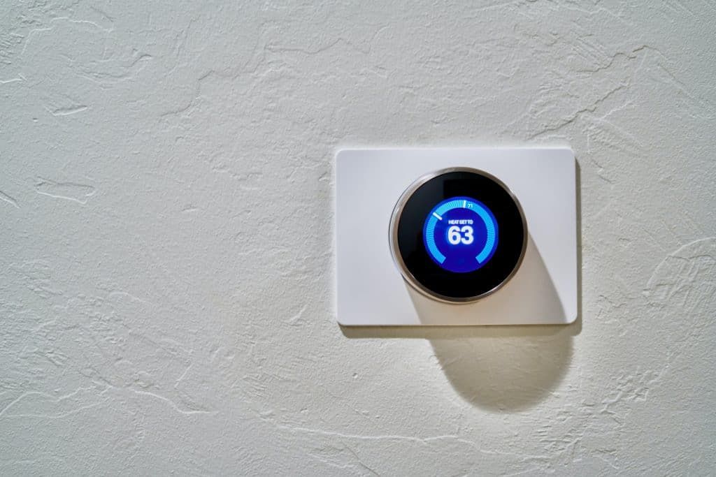 Modern thermostat displaying a temperature setting on a textured white wall.