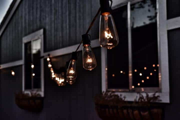 Warm LED string lights hang outside a house at dusk.